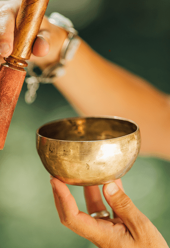 Hands holding a singing bowl and mallet.