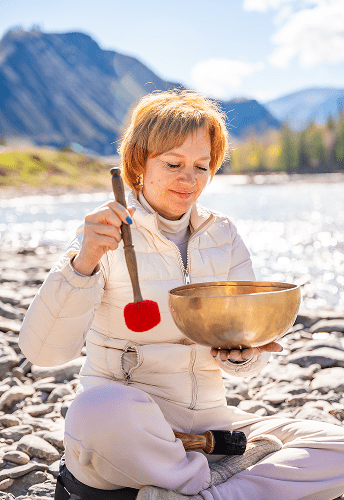 Woman playing singing bowl by riverside.